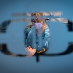 Cara attending to her client, viewed through a frosted or semi-transparent surface.
