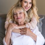 Senior woman with granddaughter hugging on settee after SPMU treatment.