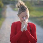 A female wearing a red jumper who is having a seasonal allergic reaction.
