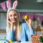 A young blonde woman puts easter eggs in an Easter basket.